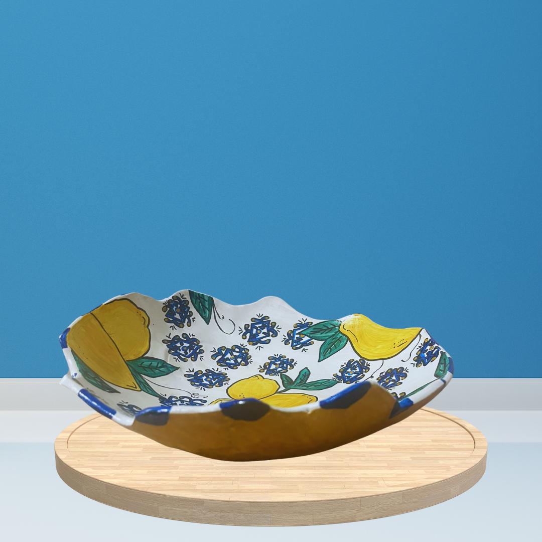 Hand-painted ceramic bowl with white base, wavy edge, and colorful lemon and floral design, including yellow lemons, blue patterns and green leaves.