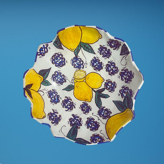 Hand-painted ceramic bowl with white base, wavy edge, and colorful lemon and floral design, including yellow lemons, blue patterns and green leaves.